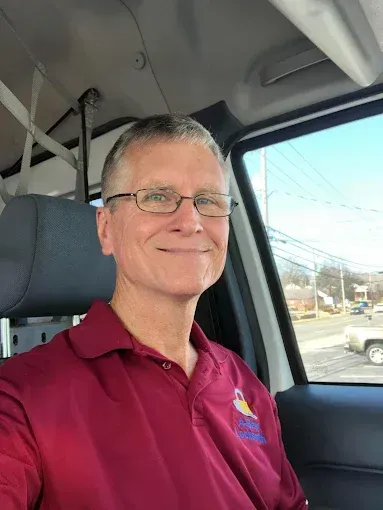 Man wearing maroon polo shirt and glasses sitting in vehicle cab