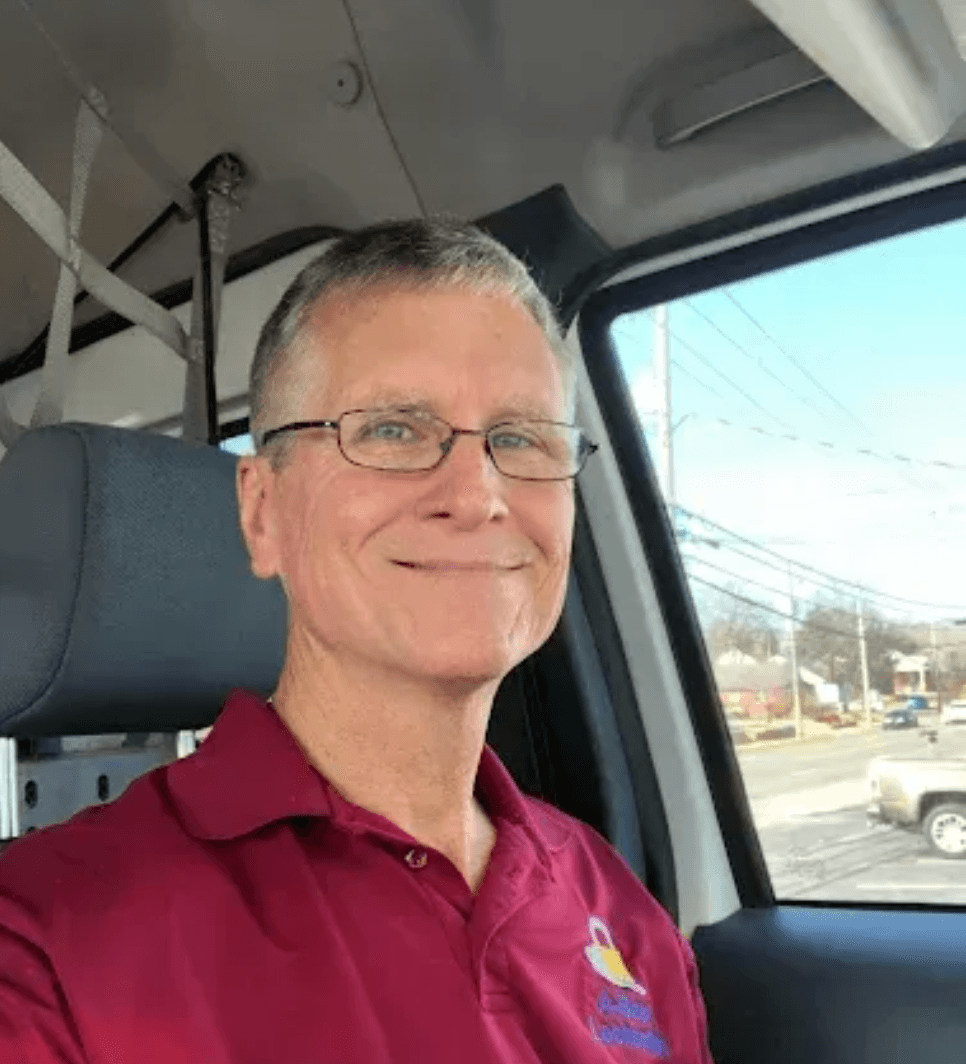 Man wearing glasses and maroon polo shirt smiling in vehicle cab