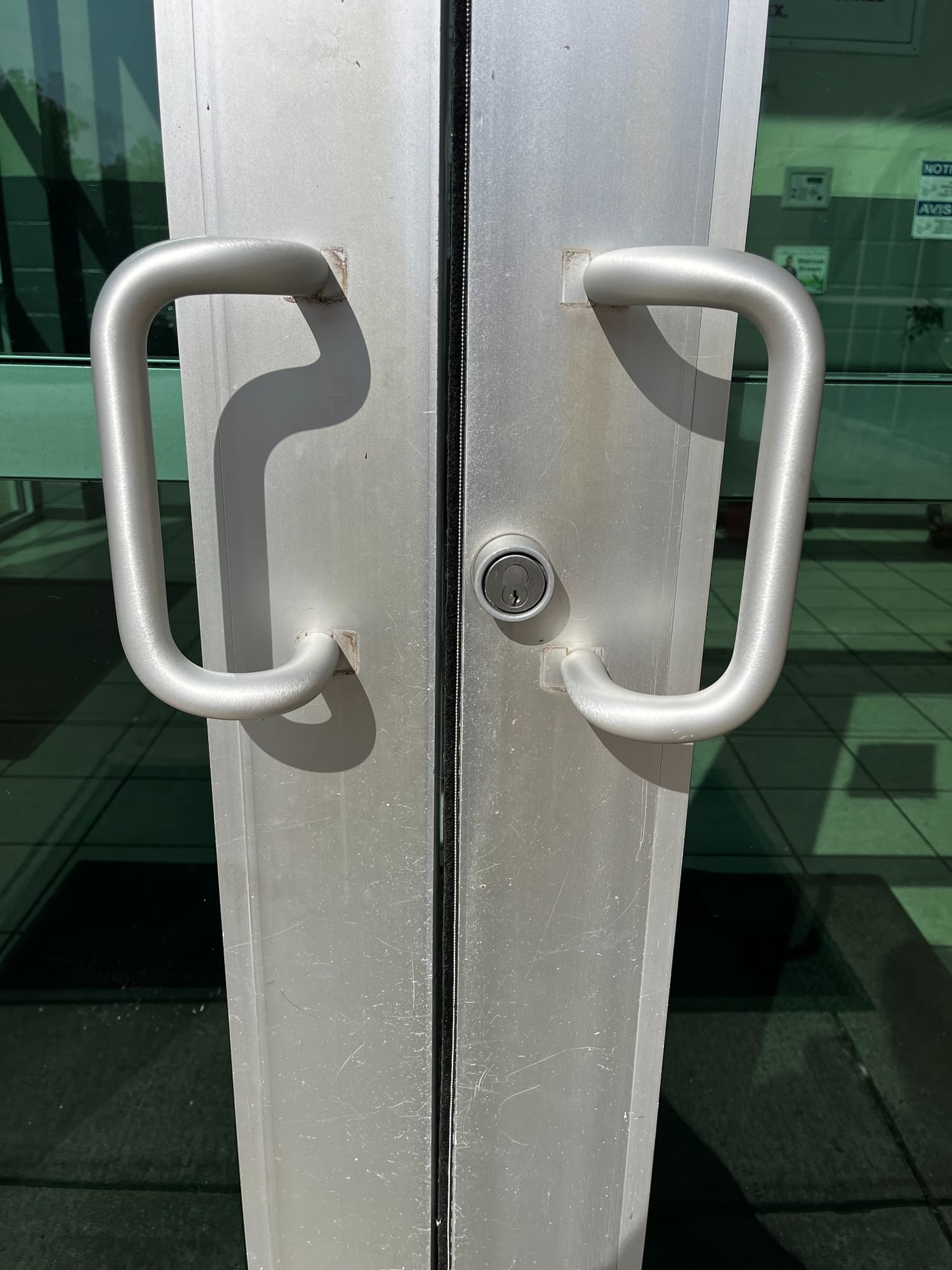 Pair of brushed aluminum push-pull handles on glass double doors with lock cylinder